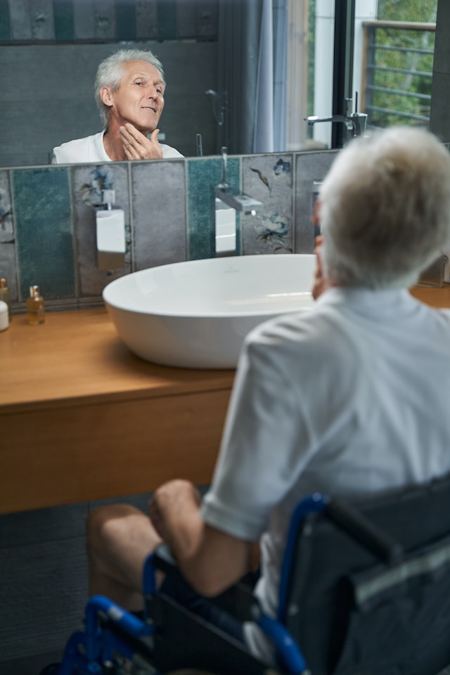 man in a wheelchair looking into a bathroom mirror